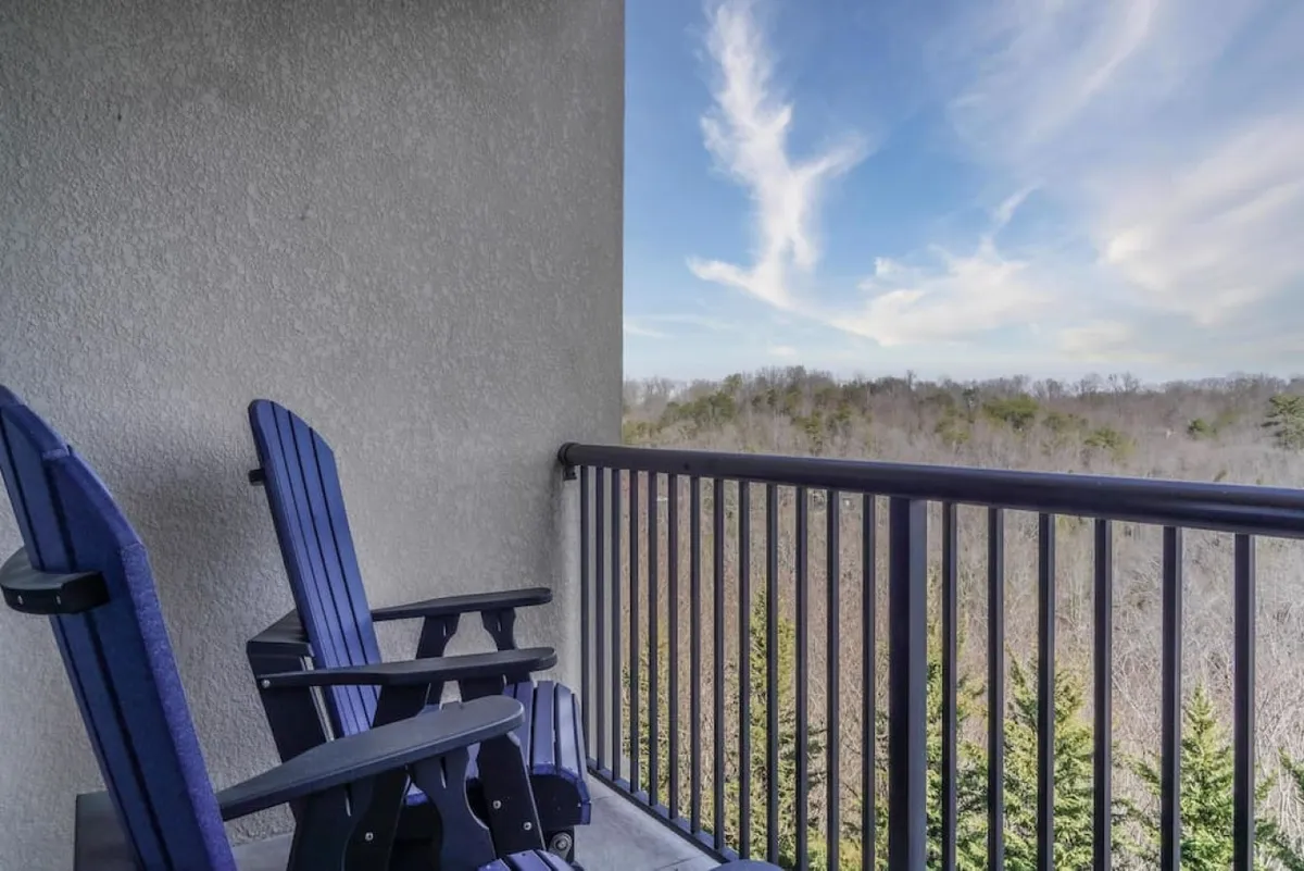 A serene balcony with comfortable chairs overlooks a lush landscape and clear blue sky. The setting invites guests to relax, socialize, or simply enjoy the outdoors without leaving the building.