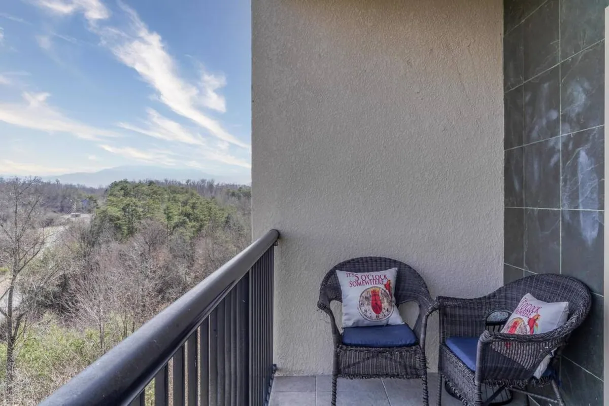 A pair of comfortable wicker chairs adorned with decorative pillows sit on the balcony, facing an unobstructed view of the mountains. The image conveys a sense of calm and encourages guests to enjoy moments of relaxation while admiring the landscape.
