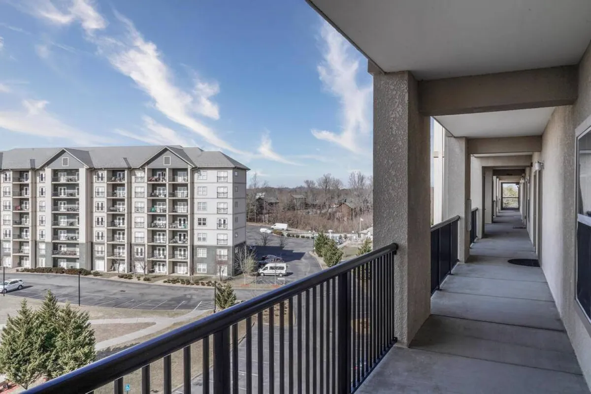 A tranquil exterior shot featuring a balcony railing, an adjacent building, and a sky dotted with clouds. The scene suggests relaxation after a day of exploring with views that connect to the outdoors.