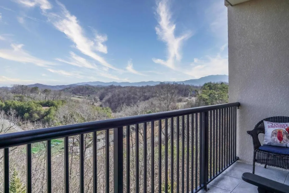 A tranquil balcony scene with a lone chair, decorative cushion, and a stunning mountain view framed by the balcony railing. The mood is peaceful, capturing the essence of sunrise coffee moments or sunset reflections.
