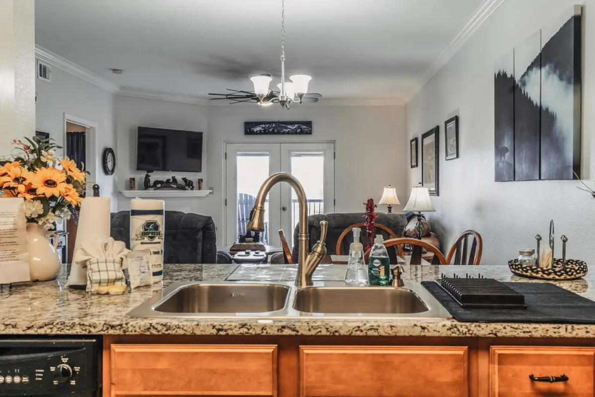 A bright, open-concept space displaying the kitchen, living room seating, a large television, and doors that open to the outdoors. The arrangement is perfect for both socializing and relaxing, aligning with the idea of gathering for movie nights or sharing stories. The living room area is visible, and the flow to the balcony is seamless.