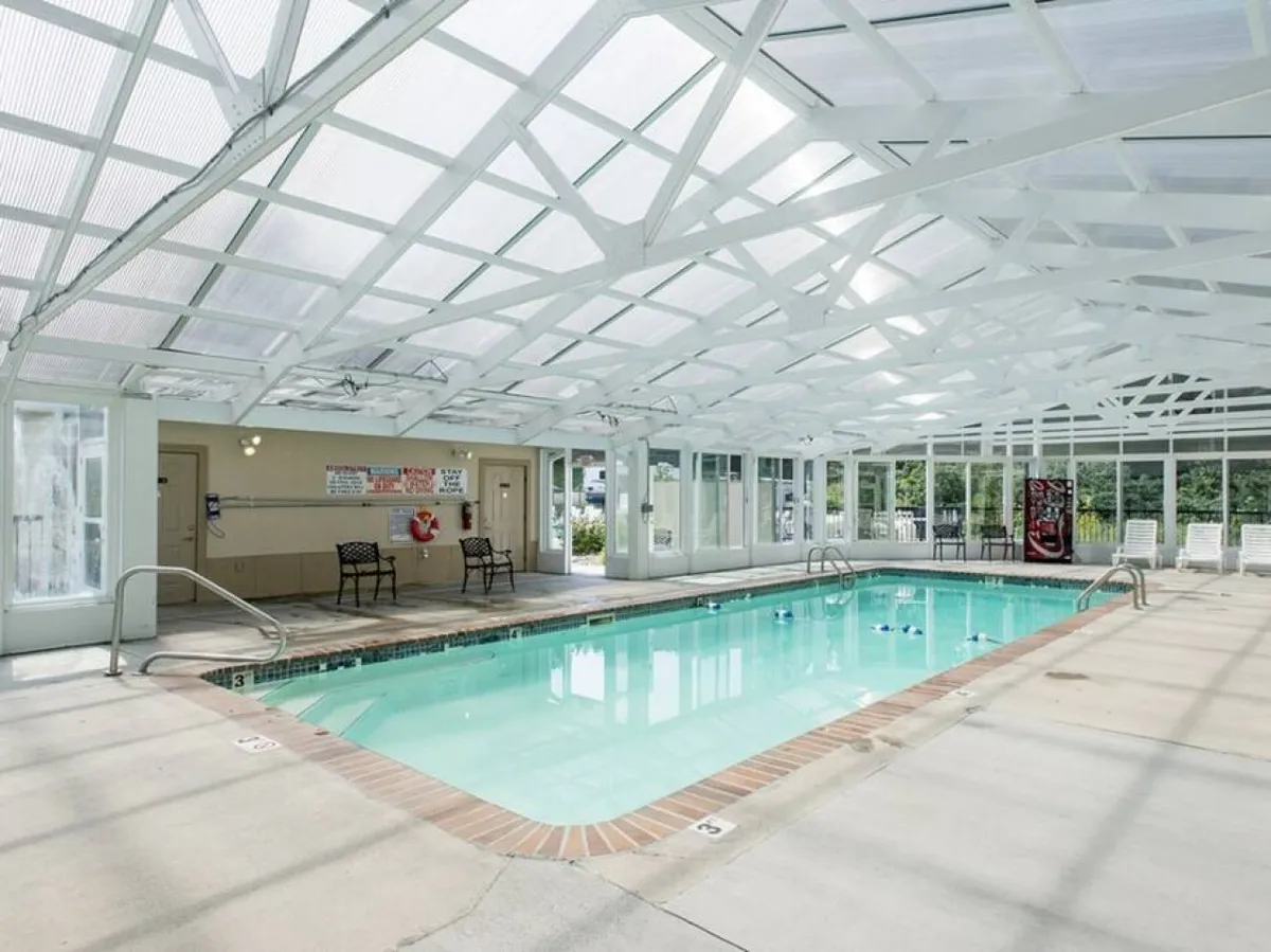 This image showcases the bright indoor swimming pool, featuring a white truss ceiling, lounge chairs, and a lifeguard station. The scene is lively and inviting, with clear water and plenty of space for swimming or relaxing by the poolside.