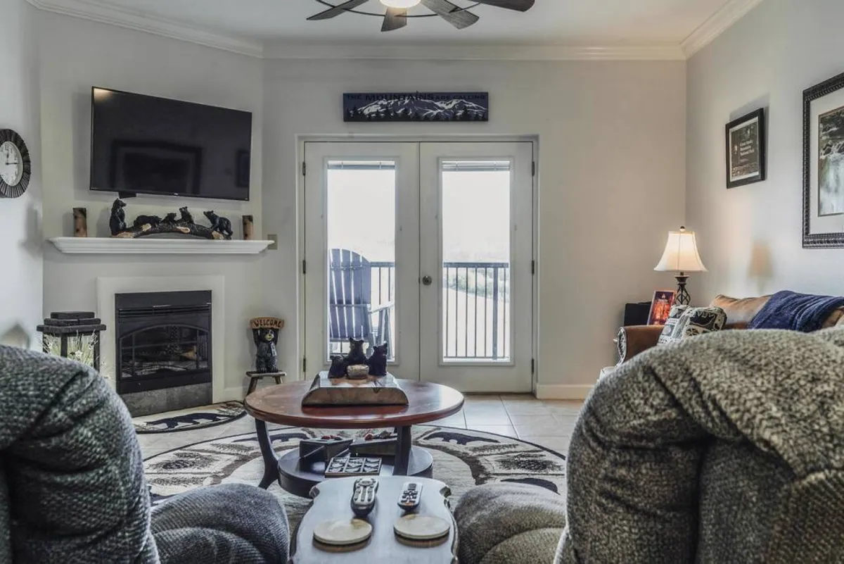 A cozy interior living area featuring a fireplace, coffee table, sliding doors, and comfortable armchairs. The space is inviting for relaxation, gathering with family, or enjoying views from the balcony. The sliding doors hint at an easy transition between indoor comfort and outdoor scenery, making it relevant for all seasons.